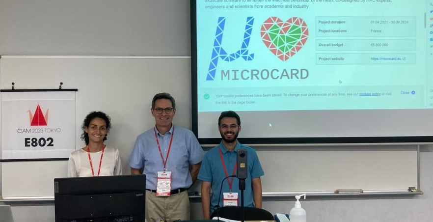 Sofia Botti, Luca Pavarino,
	 and Edoardo Centofanti in front of the MICROCARD logo at the ICIAM
	 meeting in Tokyo.